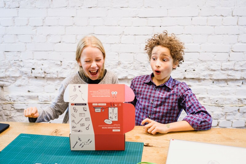 E! Ein Junge und ein M&auml;dchen &ouml;ffnen voller Staunen eine T&uuml;ftelBox.