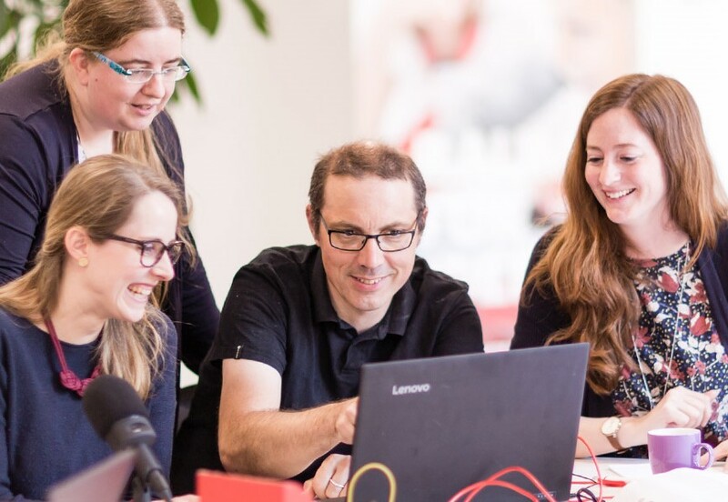 Ein Mentor schaut mit Fortbildungsteilnehmer*innen auf einen gemeinsam genutzten Latptop.