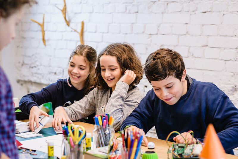 Drei Kinder sitzen an einem Tisch und spielen mit kleinen Ozobot Robotern.