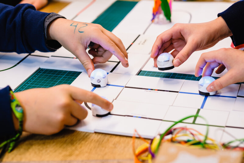 Nahaufnahme von vier Händen die kleine Ozobot Roboter auf einen Tisch stellen.
