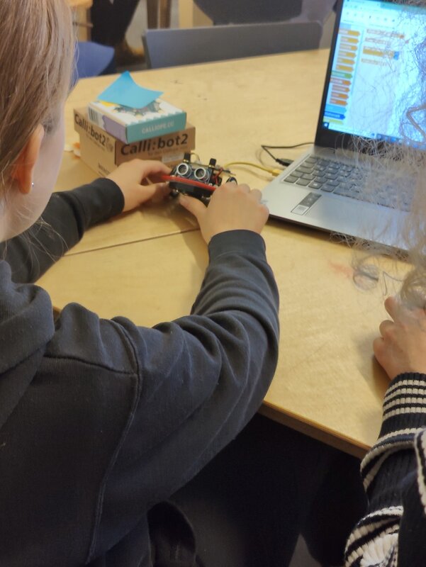 Ein Kind sitzt vor einem Laptop und hat einen selbstgebauten Roboter in der Hand.