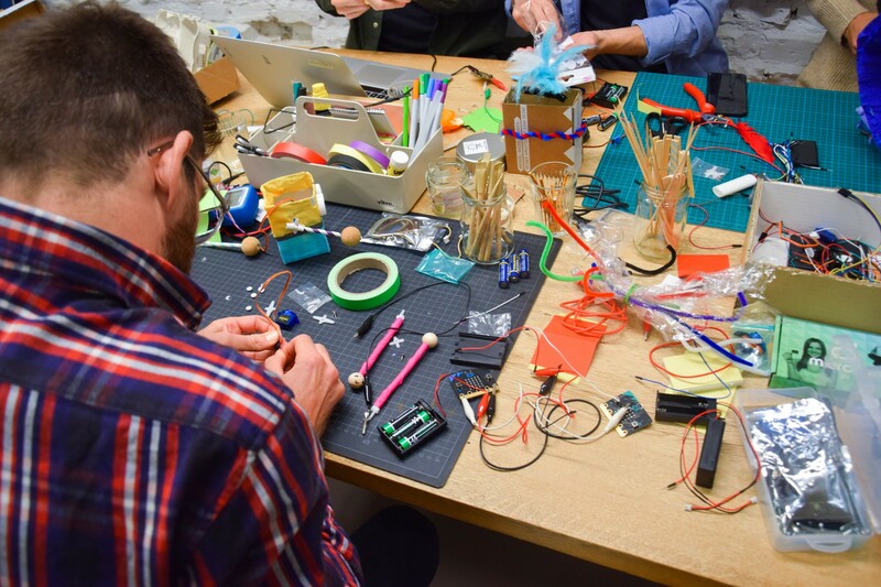 Tisch mit Bastelutensilien und digitalen Werkzeugen.
