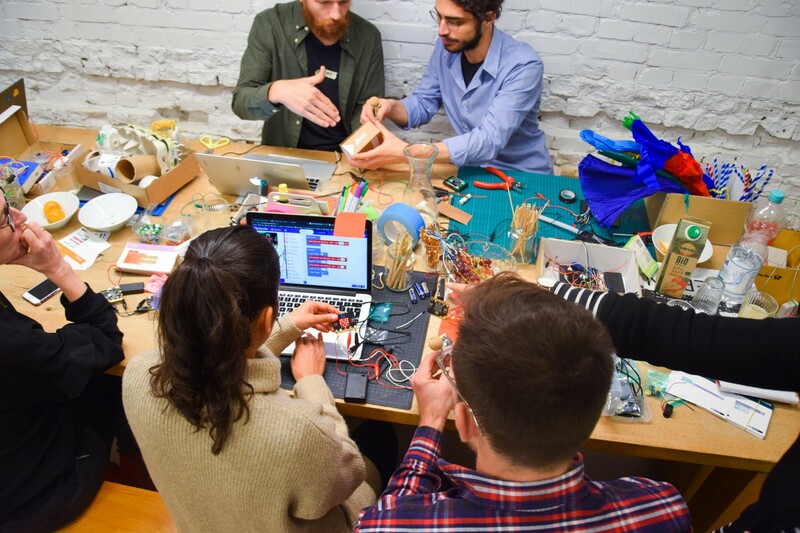 Menschen am Tisch mit Bastelutensilien, digitalen Werkzeugen, Laptop