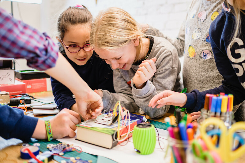 E! Eine Gruppe Kinder steckt grinsend Krokoklemmen an ein Harry Potter-Buch f&uuml;r ihr T&uuml;ftelprojekt.